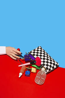 Studio shot of female hand touching cosmetics falling out of checked purse - RDTF00043