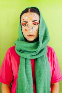 Frau mit Edelsteinaufklebern im Gesicht trägt grünen Schal vor grünem Hintergrund - EGHF00849