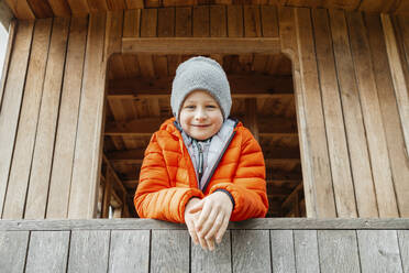 Lächelnder Junge lehnt am Holzgeländer einer Hütte - ELMF00016