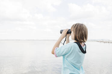 Girl looking at lake through binoculars - ELMF00021