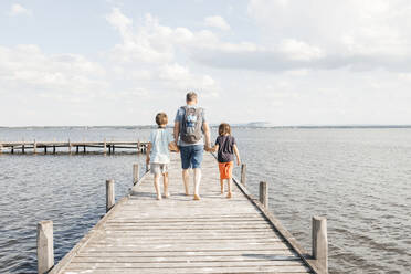 Vater geht mit Söhnen auf einem Holzsteg am See spazieren - ELMF00023