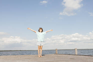 Girl standing with arms outstretched on wooden pier at lake - ELMF00025