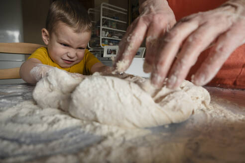 Boy kneading dough with grandmother in kitchen at home - KVBF00029