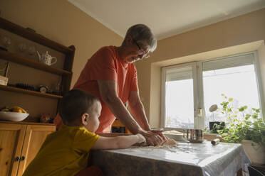 Junge hilft Großmutter beim Kneten von Teig in der Küche zu Hause - KVBF00030