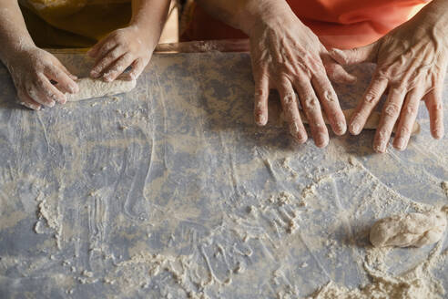 Grandson and grandmother rolling dough on kitchen island at home - KVBF00033