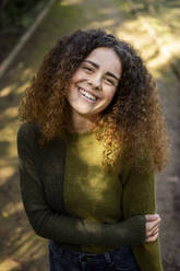 Happy woman with curly hair standing at park - LMCF00927
