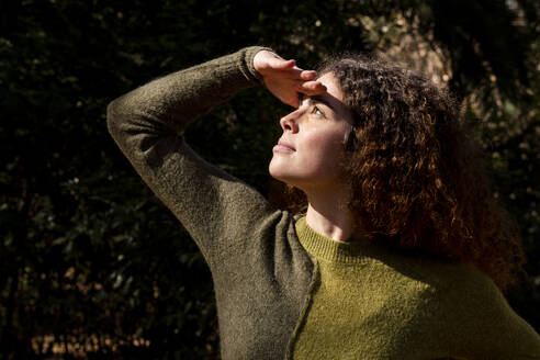 Junge Frau schützt ihre Augen im Park vor der Sonne - LMCF00935