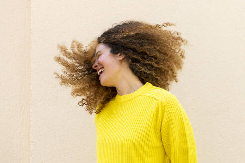 Fröhliche Frau, die sich vor einer Wand die Haare wirft - LMCF00938