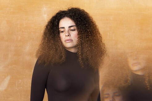 Young woman with curly hair standing against brown background - LMCF00945