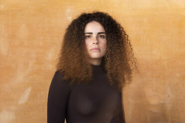 Ernste Frau mit lockigem Haar vor braunem Hintergrund - LMCF00946