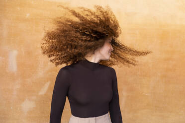 Verspielte Frau, die sich die Haare vor einem braunen Hintergrund zuwirft - LMCF00953