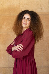 Young woman with curly hair standing in front of wall - LMCF00960