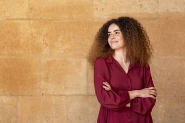 Smiling woman standing with arms crossed in front of brown wall - LMCF00961