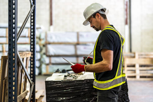 Worker wearing hardhat and examining documents at warehouse - DLTSF03785