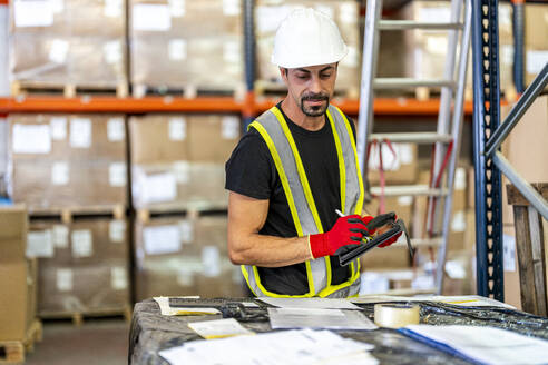 Worker examining documents with tablet PC at warehouse - DLTSF03792