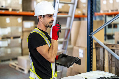 Worker talking on walkie-talkie and holding tablet PC at warehouse - DLTSF03793