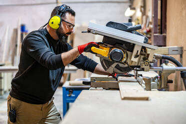 Carpenter cutting wooden plank with electric saw - DLTSF03809