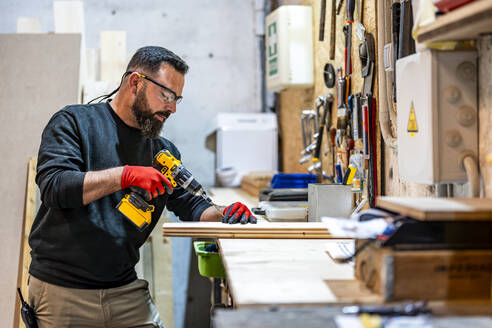 Carpenter using drill machine on wooden plank at workshop - DLTSF03811