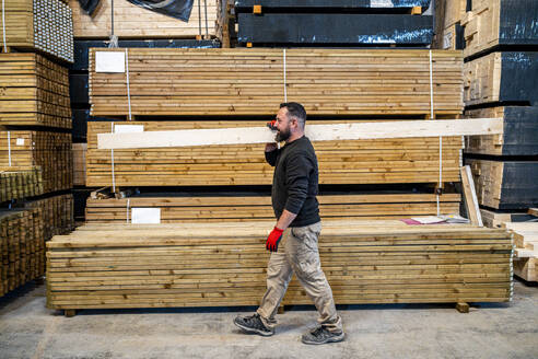 Worker carrying wooden plank at warehouse - DLTSF03820