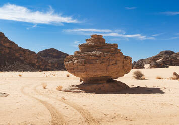 A solitary rock formation stands tall amidst a vast desert landscape under a clear blue sky in the Tadrart Rouge region - ADSF52983