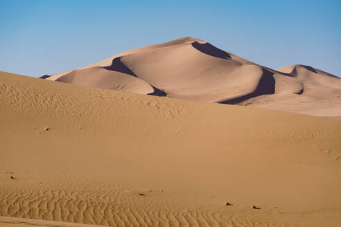 Expansive Saharan sand dunes with soft shadows and a clear blue sky backdrop in the Erd D'Admer region - ADSF52987
