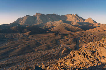 Sunrise bathes Mount Tazat in warm golden light, highlighting the textured landscape of rocky outcrops and winding paths - ADSF52989