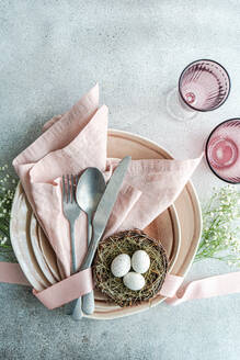 From above aesthetically pleasing Easter table arrangement featuring a nest with speckled eggs, nestled on stacked ceramic plates with a pink linen napkin. - ADSF53001