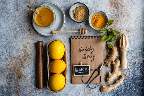 An array of fresh cooking ingredients including lemons, honey, ginger, and spices, alongside a notebook labeled Healthy Cooking on a textured tabletop - ADSF53005