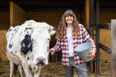 Portrait of a smiling young farmer woman with a dairy cow. Animal welfare and care on an organic farm. - ADSF53022