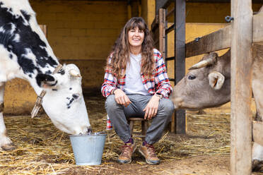 Porträt einer lächelnden jungen Bäuerin mit einer Milchkuh. Tierschutz und -pflege auf einem Biobauernhof. - ADSF53024