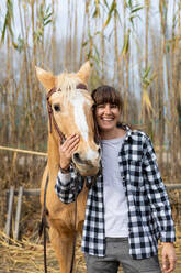 Junge Reiterin umarmt ihr braunes Pferd in einem Reitsportzentrum - ADSF53033