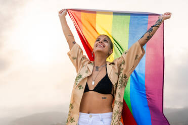 Beautiful lesbian woman holding LGBT flag at the beach, concepts about LGBTQ community, diversity, love and lifestyle - DMDF10246