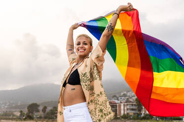 Beautiful lesbian woman holding LGBT flag at the beach, concepts about LGBTQ community, diversity, love and lifestyle - DMDF10247