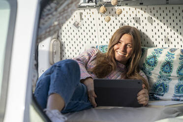Lächelnder Freiberufler mit Tablet-PC liegend im Wohnmobil - JSIF00004