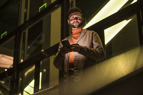 Smiling man holding smart phone at night - UUF31523