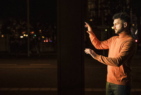 Man using touch screen kiosk on street at night - UUF31537