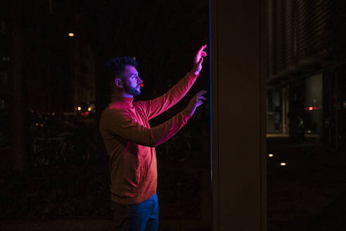 Man using touch screen kiosk machine on street at night - UUF31538