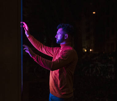 Man wearing red t-Shirt and touch screen kiosk at night - UUF31539