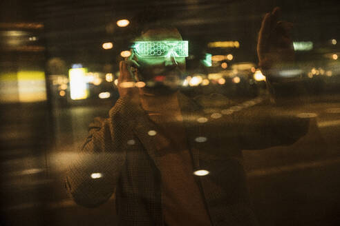 Man wearing smart glasses gesturing behind glass pane - UUF31547