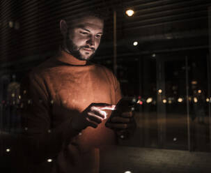 Man using smart phone seen through glass at night - UUF31553