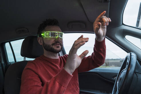 Man wearing smart glasses and gesturing inside car - UUF31556