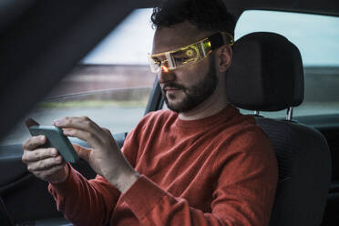 Man wearing smart glasses and using smart phone in car - UUF31560