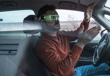 Man wearing green colored smart glasses gesturing in car - UUF31563