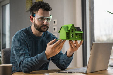 Architect wearing smart glasses and examining model house - UUF31578