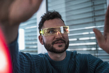 Smiling man wearing smart glasses and gesturing at home - UUF31589