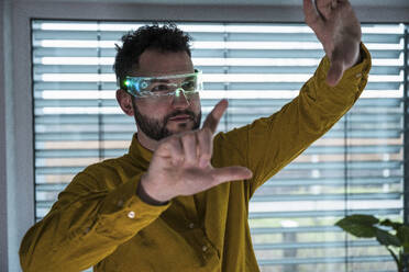 Man wearing smart glasses and gesturing in front of window - UUF31595