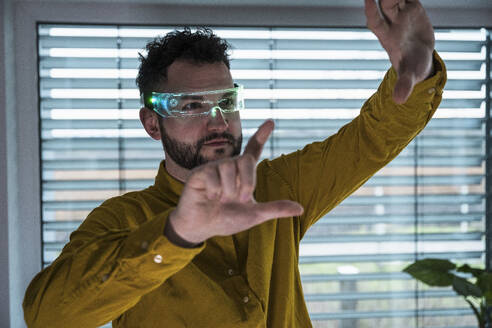 Man wearing smart glasses and gesturing in front of window - UUF31595