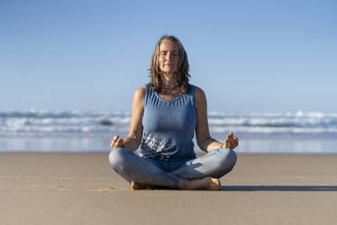 Mature woman sitting in lotus position on sand at beach - JSIF00010