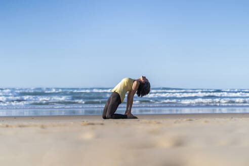 Ältere Frau übt Kamel-Yoga-Pose am Strand - JSIF00014
