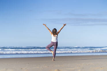Frau in Baum-Yoga-Pose mit erhobenen Armen am Strand - JSIF00016